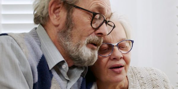 Ett äldre par sitter nära varandra i soffan